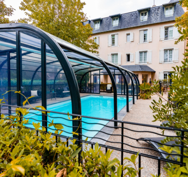 Vue sur une piscine couverte dans une cours pleine de verdure avec un batiment en arrière plan